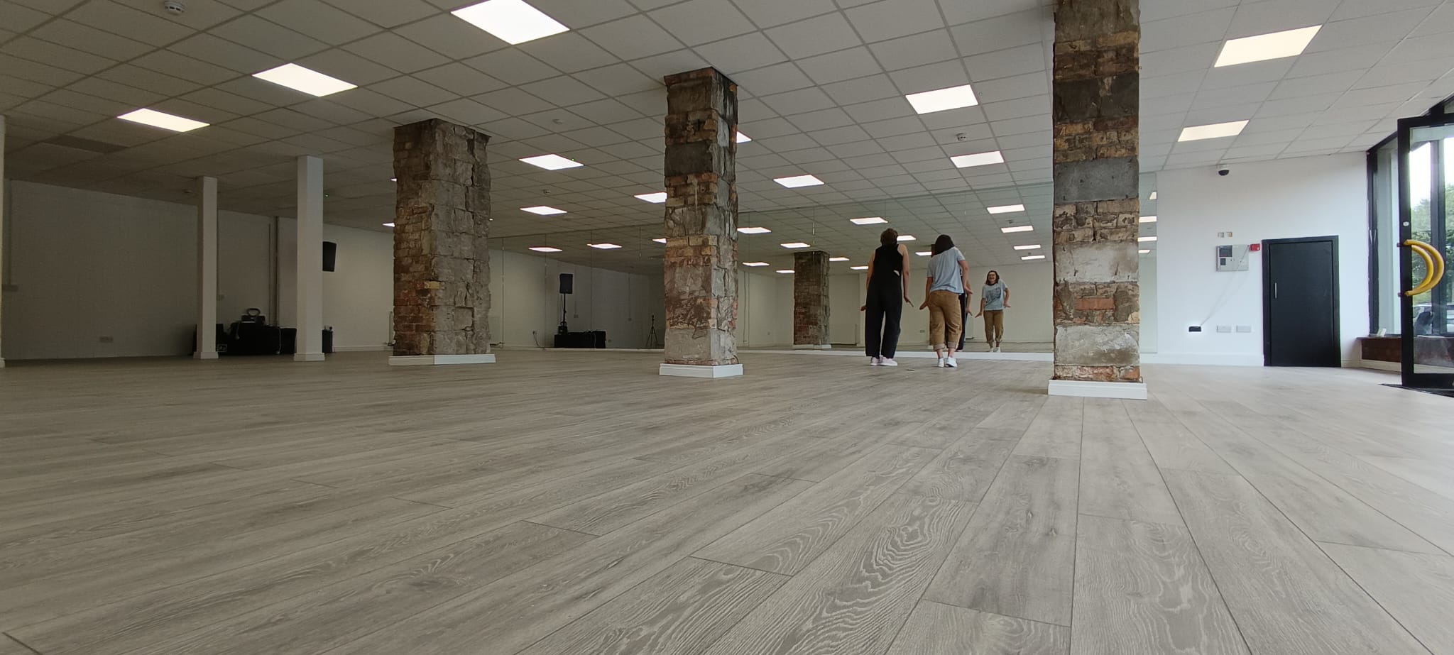 The new Peters Hill room: a long, empty wood floor running away from the camera between exposed brick columns, three people walking across it in the distance.